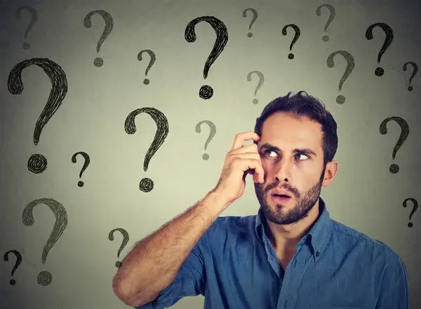 A man holding his head with many question marks above him.